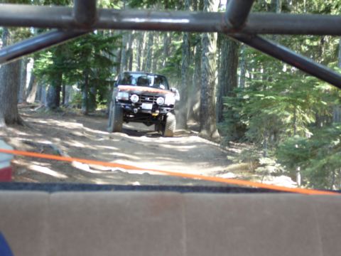 1991 Ford Bronco - An off-road vehicle navigates a dusty trail through a dense forest.