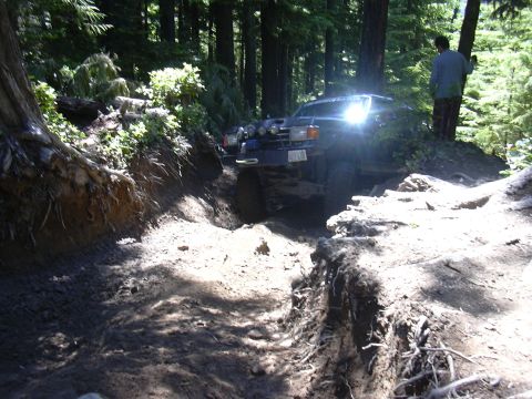 1991 Ford Bronco - An off-road vehicle tackles a challenging, muddy path surrounded by dense trees.