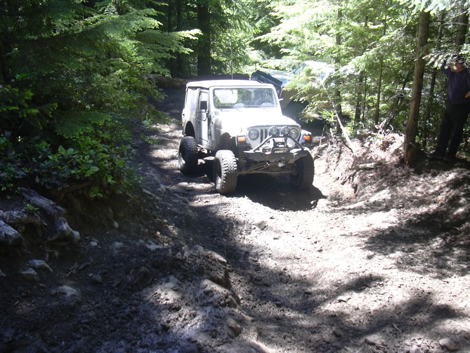 White Jeep Wrangler with off-road tires and winch on a muddy forest trail