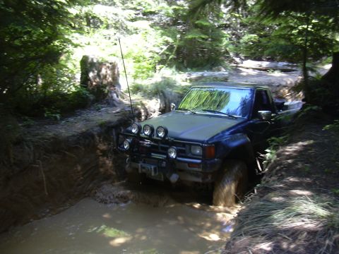 1991 Ford Bronco - Toyota pickup truck navigating a muddy obstacle on a wooded trail.