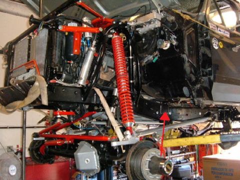 1991 Ford Bronco - The chassis of a heavily modified off-road vehicle is shown, prominent red suspension parts and an exposed engine bay.
