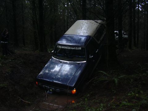 1991 Ford Bronco - A Ford Bronco navigates a muddy trail in a dense forest, with another Bronco visible in the background.