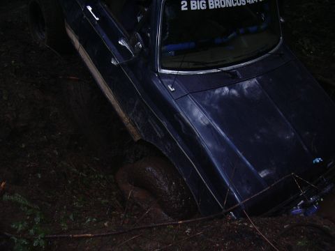 1991 Ford Bronco - A dark blue SUV is stuck in the mud, with its front right wheel deep in the mire.