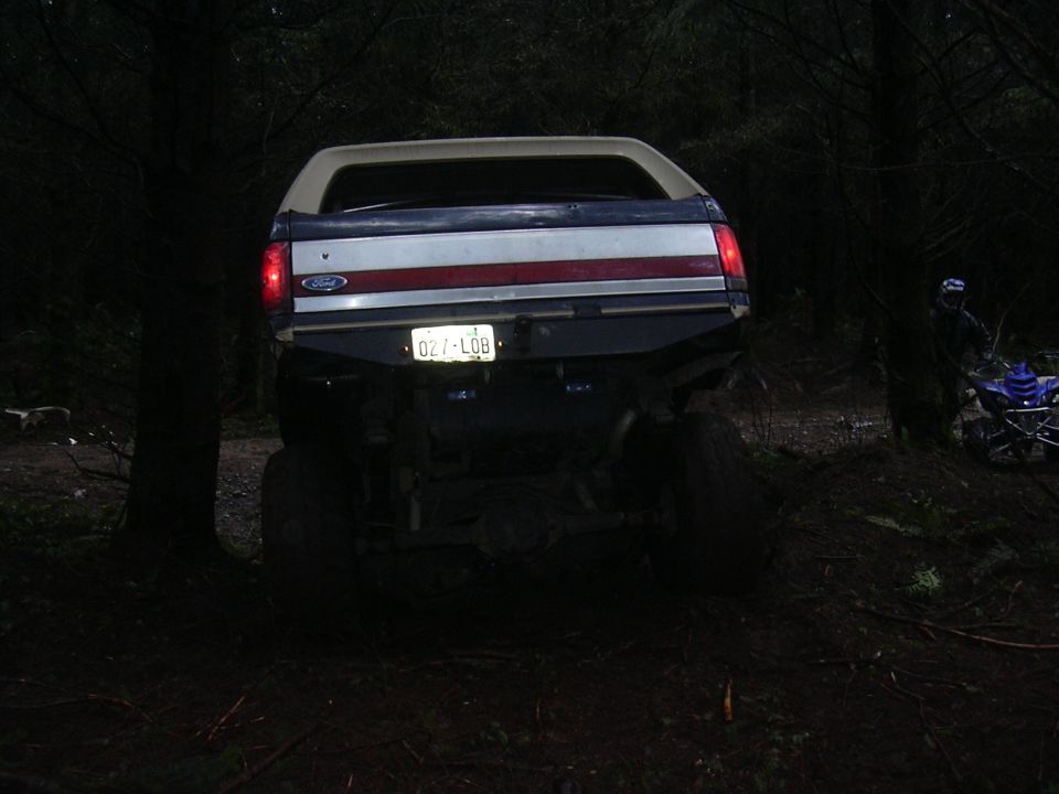 1991 Ford Bronco rear end with custom bumper and license plate 027-LOB. ATV visible to the right