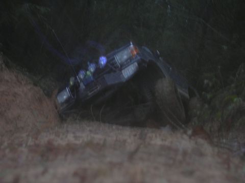 1991 Ford Bronco - A dark SUV is tilted on its side, with auxiliary lights visible on the roof, suggesting off-road use.