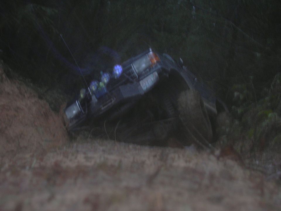 Dark SUV tilted on its side, lights on roof, off-road tires