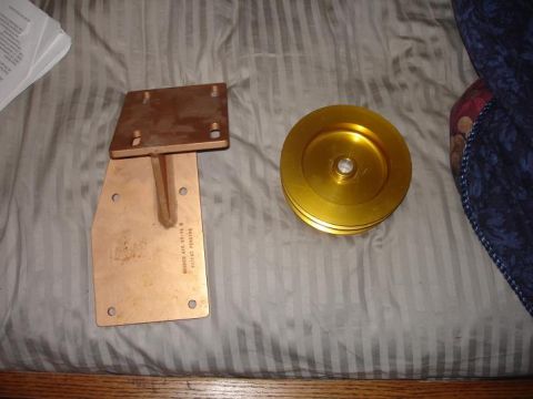 1996 Ford F-150 - A copper mounting bracket and a gold pulley are shown on a striped surface.