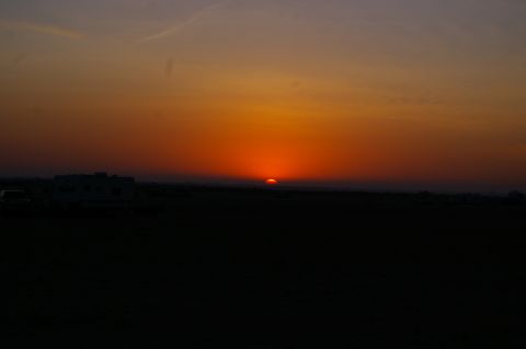 1986 Ford Bronco - Sunset over a field with a building silhouette visible against the colorful sky.