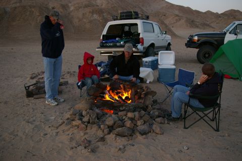 1986 Ford Bronco - A group enjoys a campfire in the desert with their vehicles and camping gear.