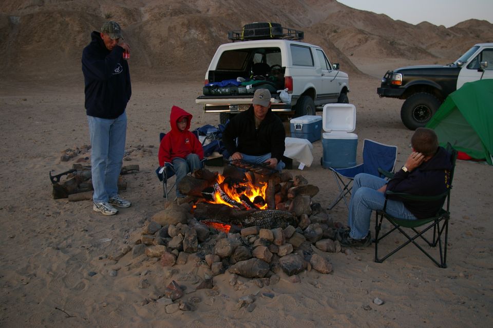 people around campfire with two SUVs and a tent in desert