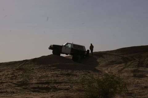1986 Ford Bronco - A two-tone Ford Bronco navigates a sandy incline under a clear sky.