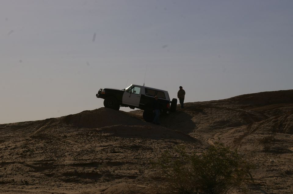 Two-tone Ford Bronco on a dirt hill with a person standing nearby
