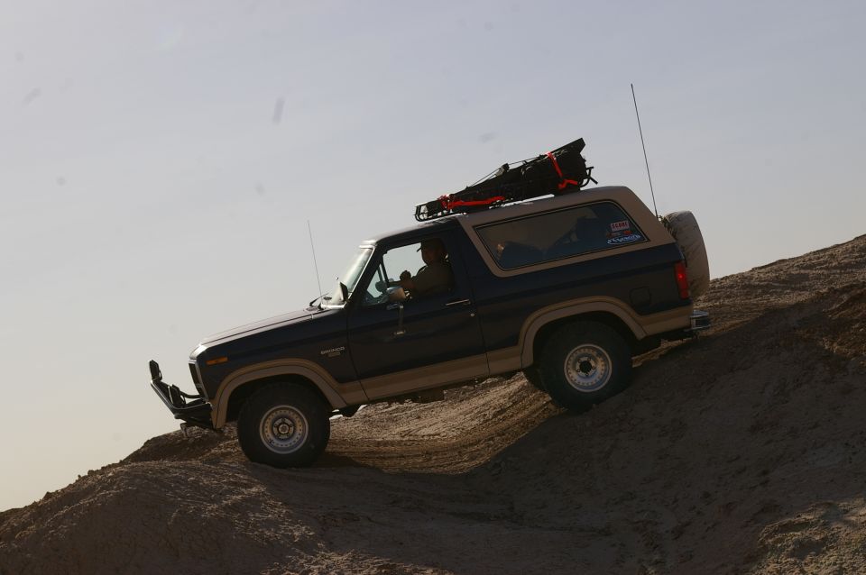 Ford Bronco driving up a sandy hill, roof rack loaded
