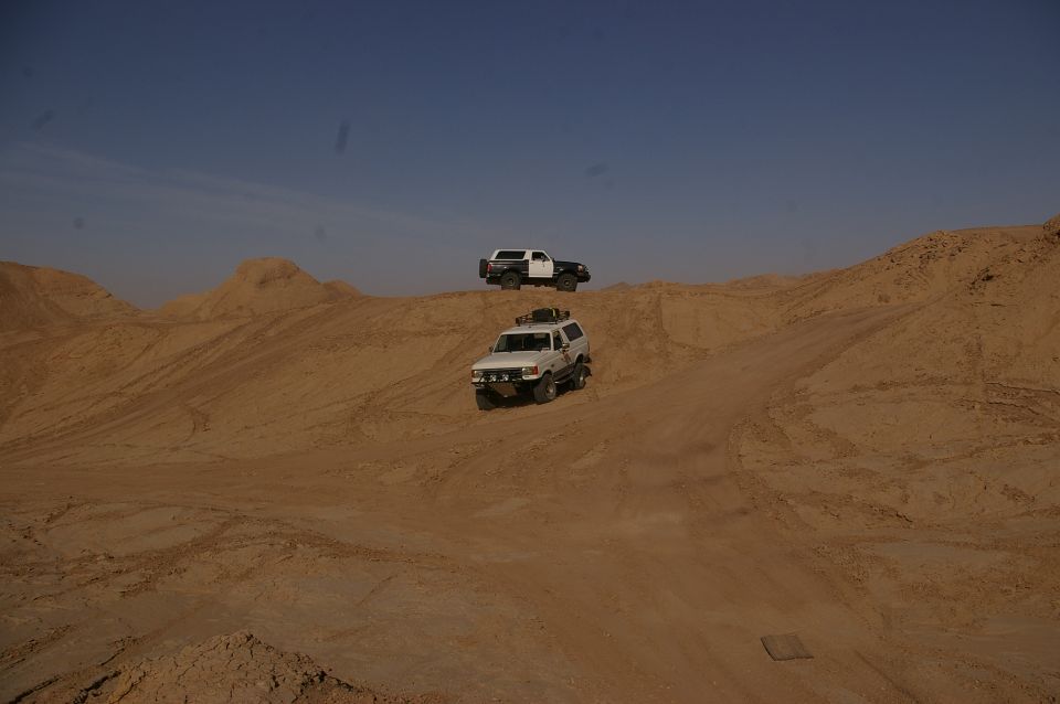 Two SUVs driving on sand dunes under a clear blue sky