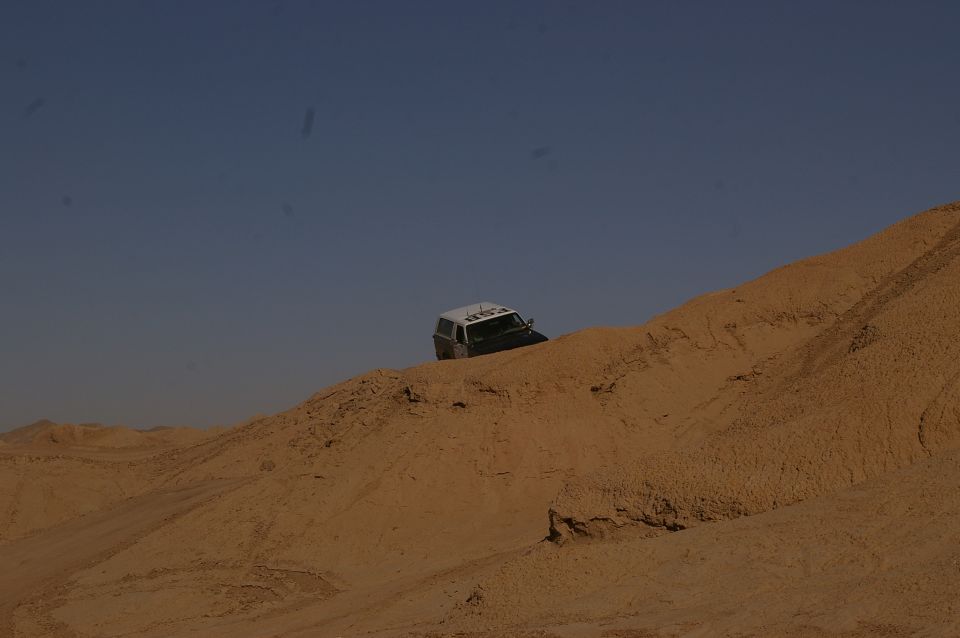 White top SUV driving on a sand dune