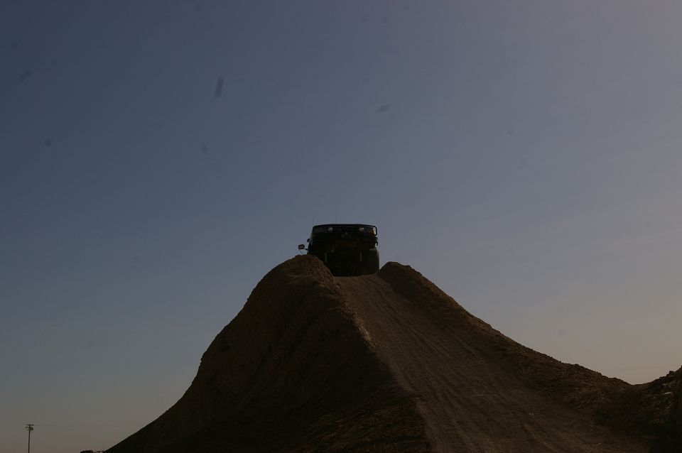 Dark SUV on top of a dirt mound against a clear blue sky