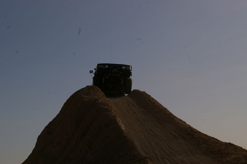 Dark 1986 Ford Bronco cresting a dirt hill against a clear sky