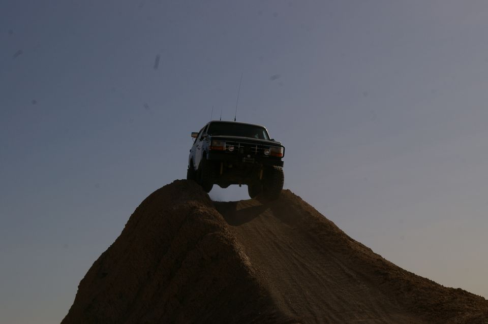 Dark-colored 1987 Ford F-150 climbing a dirt mound against a clear sky