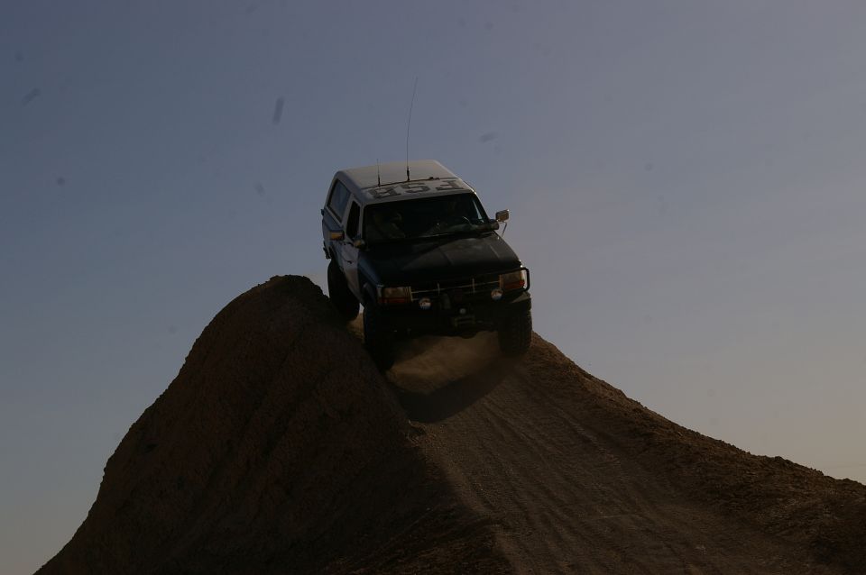 Dark SUV with white camper shell driving up a dirt mound, dust kicking up