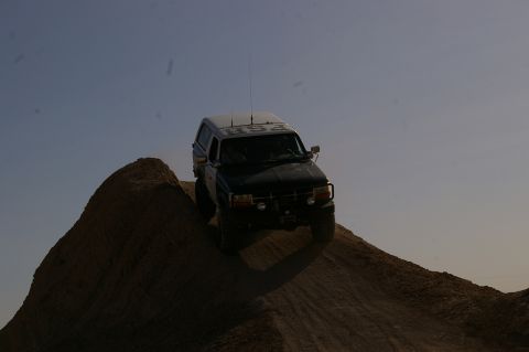 1986 Ford Bronco - This black Ford Bronco, likely a 1992 model, navigates an off-road incline under a clear sky.