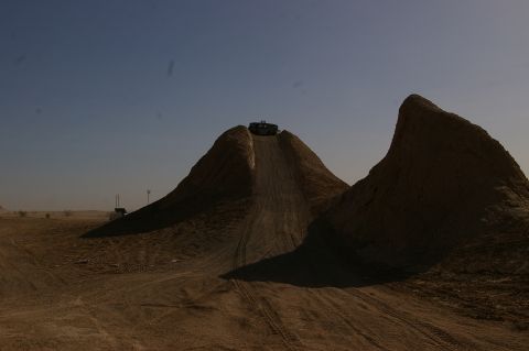 1986 Ford Bronco - A dark-colored SUV is seen from behind as it reaches the top of a steep dirt incline in a desert landscape.