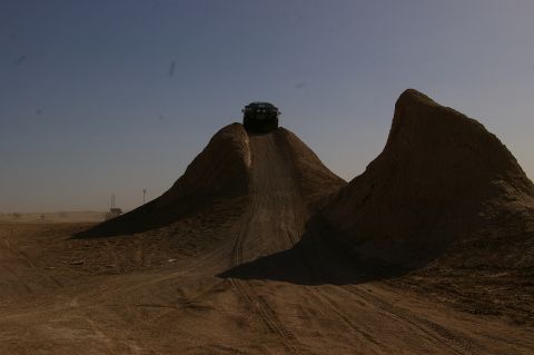 1986 Ford Bronco - A dark SUV navigates a steep dirt incline in a barren, dusty landscape under a bright sky.