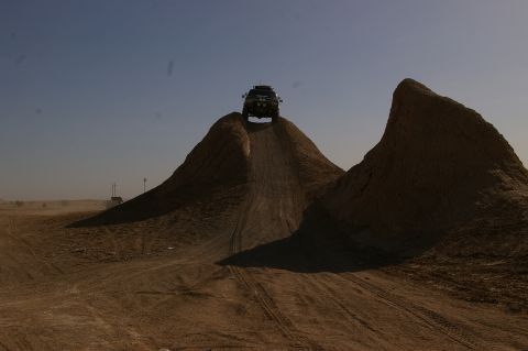 1986 Ford Bronco - An SUV navigates a steep dirt incline in a barren, dusty landscape.