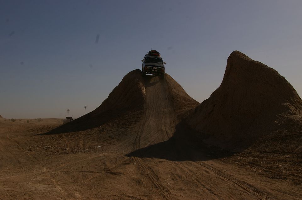 White SUV cresting a dirt hill with luggage on roof