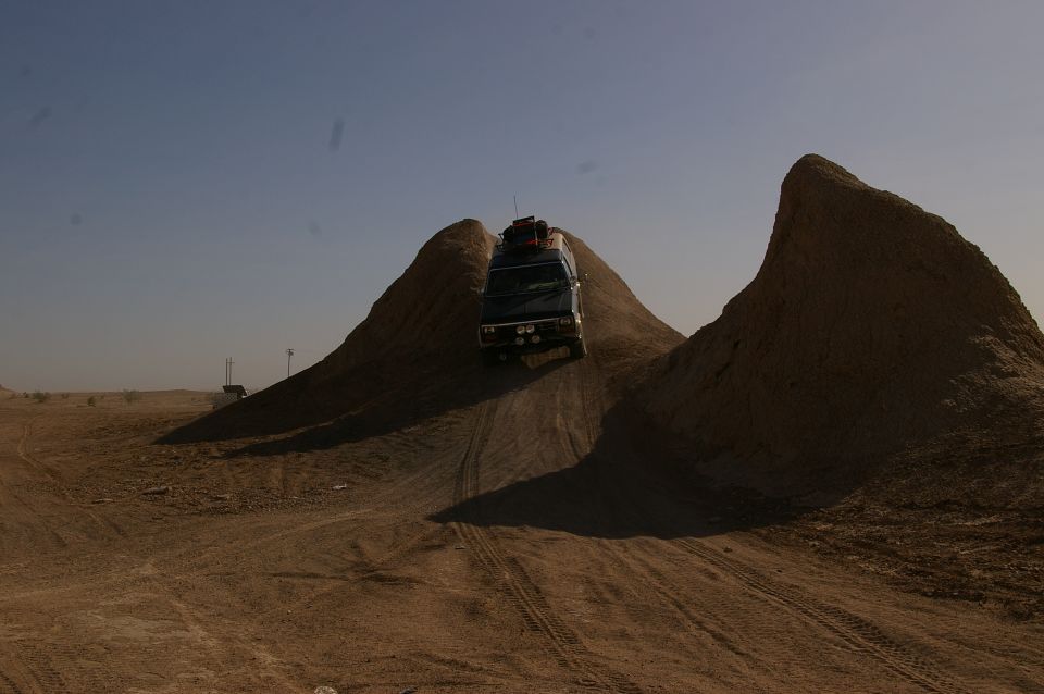 Van with luggage on roof driving up a dirt hill in a desert landscape