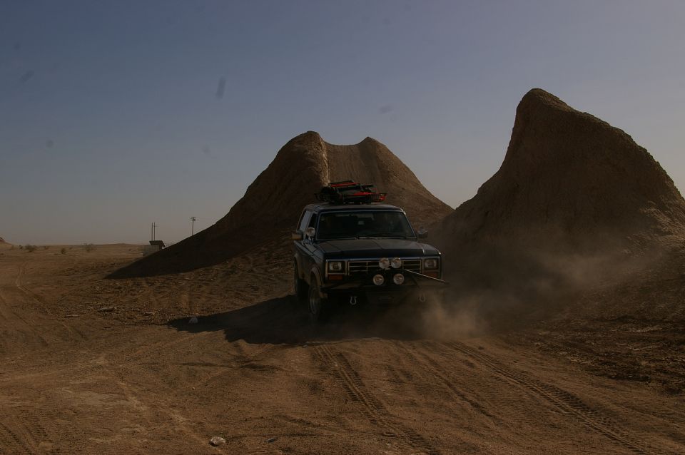 Dark blue Ford Bronco driving on a dirt road in a desert landscape with large rock formations