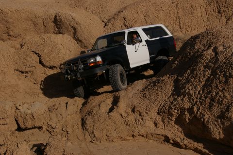1986 Ford Bronco - A two-tone Ford Bronco navigates a steep, sandy incline.