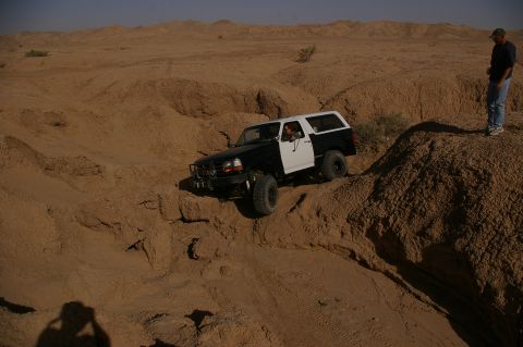 1986 Ford Bronco - Ford Bronco tackling challenging desert terrain with a driver and observer present.