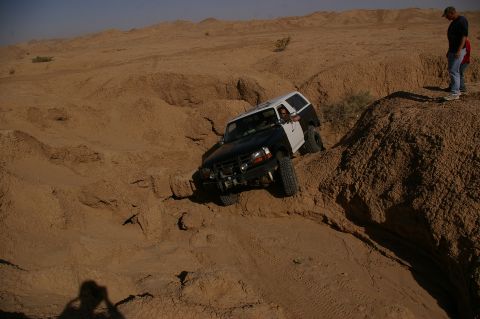 1986 Ford Bronco - An off-road SUV navigates a challenging sandy terrain, with a spectator observing from the ridge.