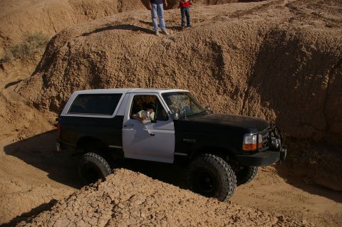 1986 Ford Bronco - A two-tone Ford Bronco navigates a challenging off-road terrain with steep, sandy inclines.