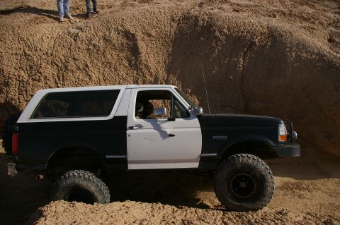 1986 Ford Bronco - A modified Ford Bronco navigates a sandy incline, its two-tone paint job contrasting with the desert landscape.
