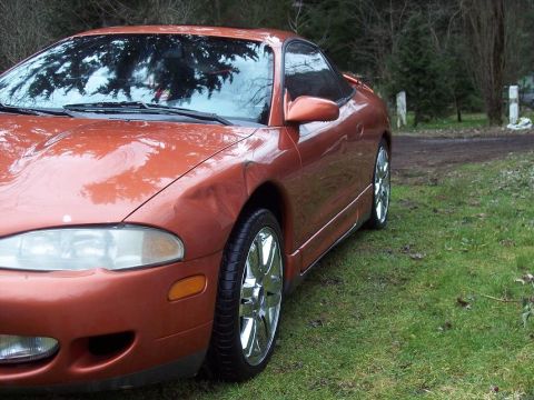 1995 Mitsubishi Eclipse - A 1995 Mitsubishi Eclipse coupe in orange with chrome wheels is seen from the front-right angle on a grassy area.