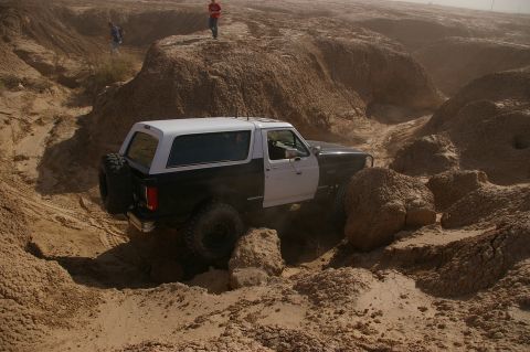 1986 Ford Bronco - Ford Bronco tackling a challenging off-road course in a desert landscape.