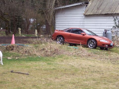 1995 Mitsubishi Eclipse - The 1995 Mitsubishi Eclipse coupe is seen from a three-quarter front view, parked on a grassy area beside a white building.