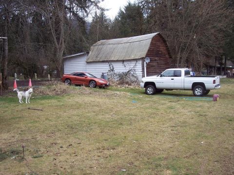 1995 Mitsubishi Eclipse - An orange sports car and a white pickup truck are parked in a grassy yard next to a barn.