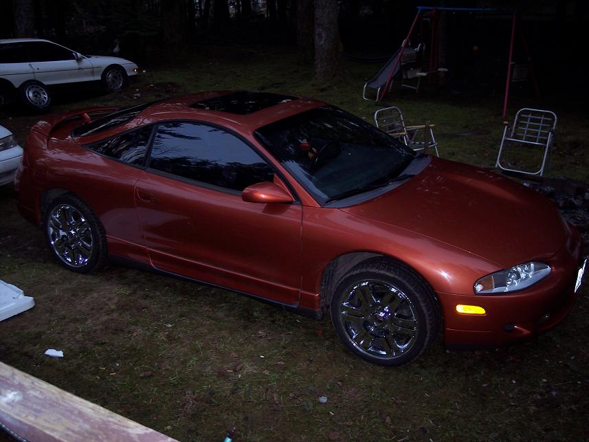 Orange 1995 Mitsubishi Eclipse coupe with chrome wheels and a sunroof, parked on grass