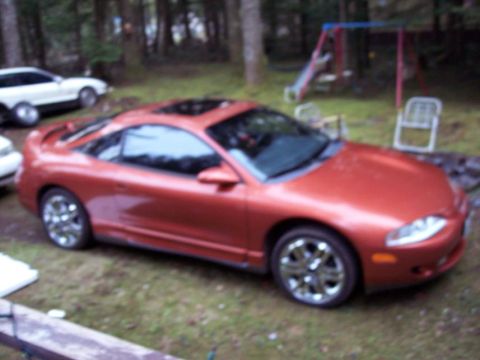 1995 Mitsubishi Eclipse - A red 1995 Mitsubishi Eclipse coupe with a sunroof is parked in a grassy yard next to a white car.