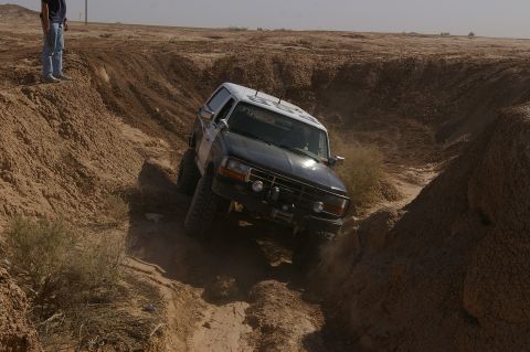 1986 Ford Bronco - Ford Bronco navigating a challenging off-road trail with steep dirt walls.