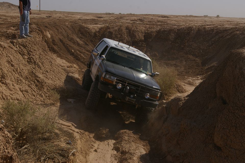 Modified Ford Bronco descending a steep dirt embankment. Lifted suspension and off-road tires are visible