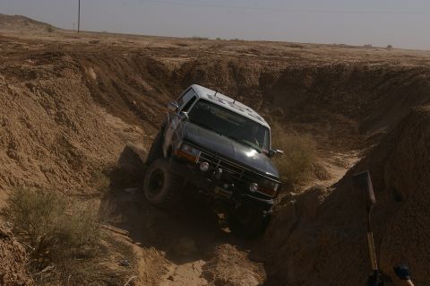 1986 Ford Bronco - A Ford Bronco navigates a challenging dirt terrain, its front end angled towards the viewer.