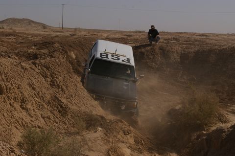 1986 Ford Bronco - A white SUV navigates a dusty off-road terrain, kicking up dirt as it descends into a trench.