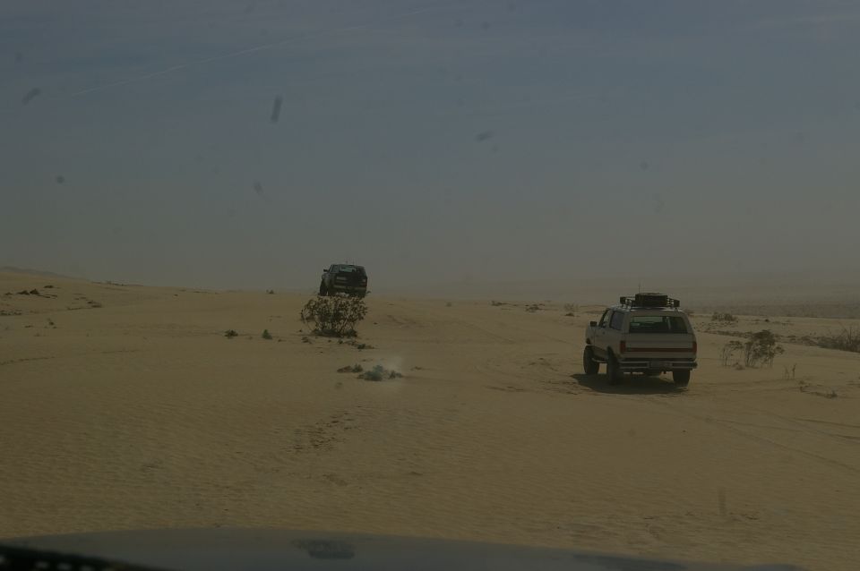 Two SUVs driving on sand dunes under a hazy sky