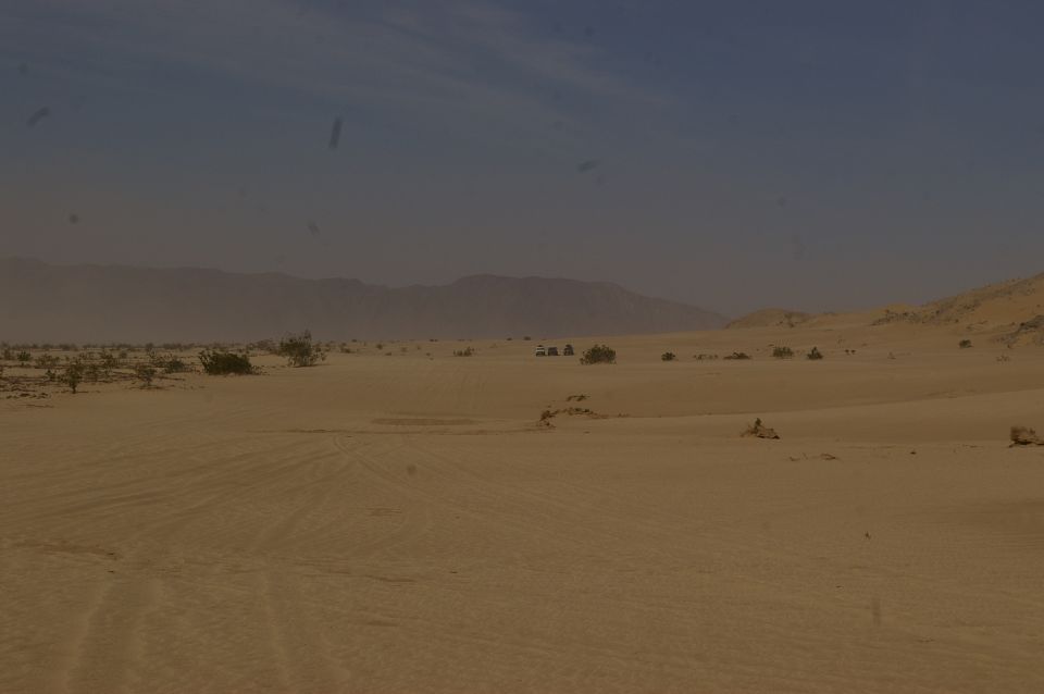 Desert landscape with tire tracks in sand and distant mountains under a hazy blue sky