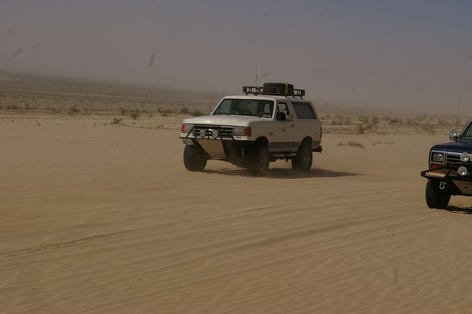 white SUV with roof rack driving in desert, another dark SUV to the right