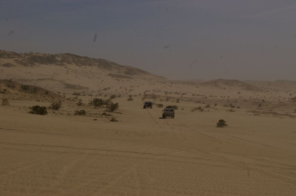 Three SUVs driving on sand dunes under a hazy sky