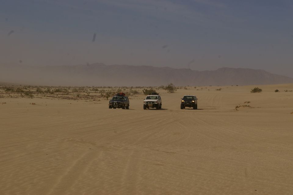 Three SUVs driving on sand dunes under a hazy sky